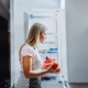 smiling-caucasian-blond-housewife-in-apron-taking-vegetables-from-fridge