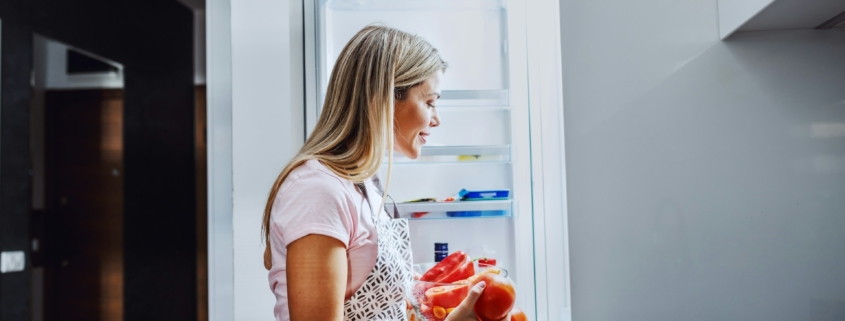 smiling-caucasian-blond-housewife-in-apron-taking-vegetables-from-fridge